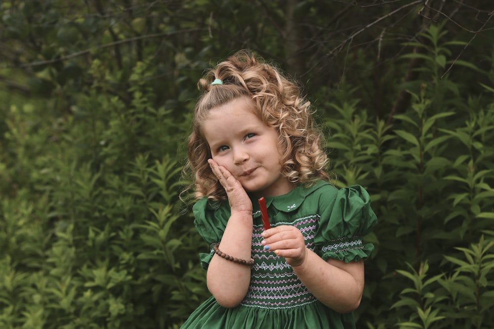 a little girl in a green dress holding a red umbrella