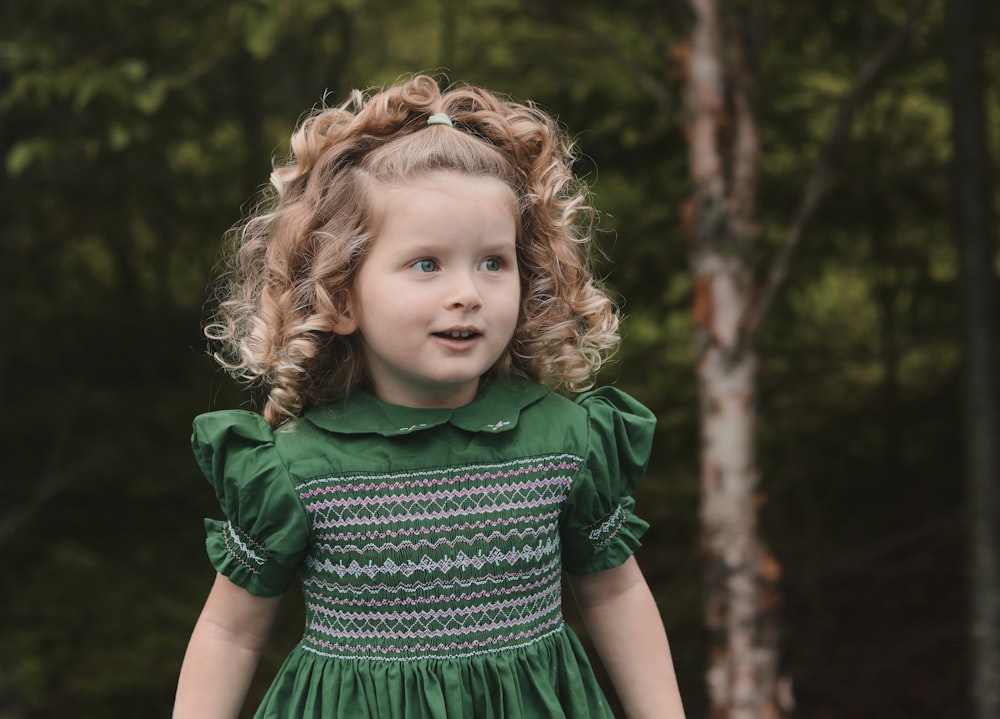 a little girl with curly hair wearing a green dress