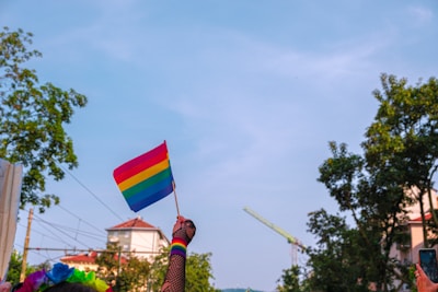 Close-up of hands holding a rainbow flag while walking on a forest trail.