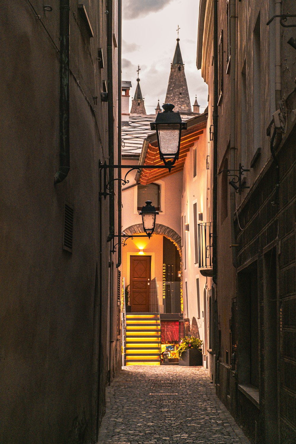a narrow alley way with a lamp post and steeple in the background