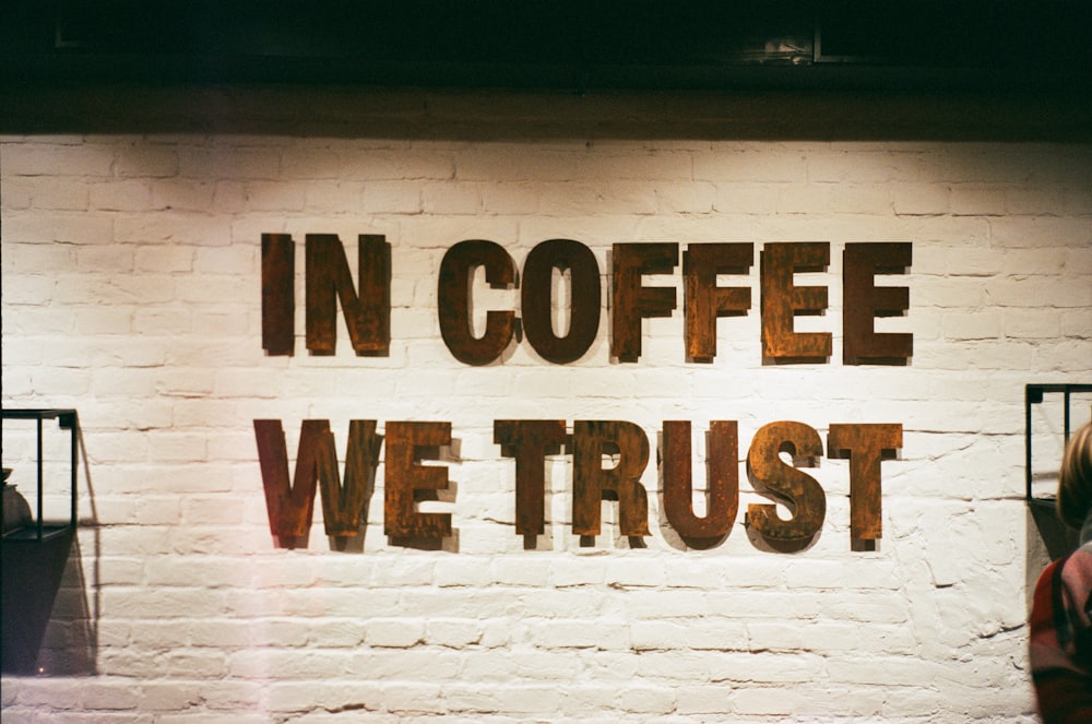 eine Ziegelmauer mit einem Schild mit der Aufschrift "In Coffee We Trust"