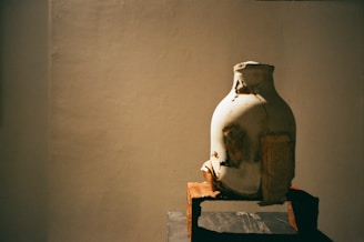 A close-up of a weathered mid-century ceramic vase sitting on reclaimed oak shelf, bathed in soft natural light.