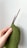A hand is holding two wooden knitting needles and working on a piece of green knitted fabric with a bumpy texture.