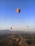 A colorful hot air balloon rising over the ancient pyramids of Teotihuacán at sunrise.