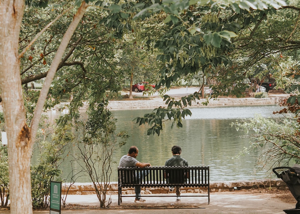 two people sitting on a bench near a body of water