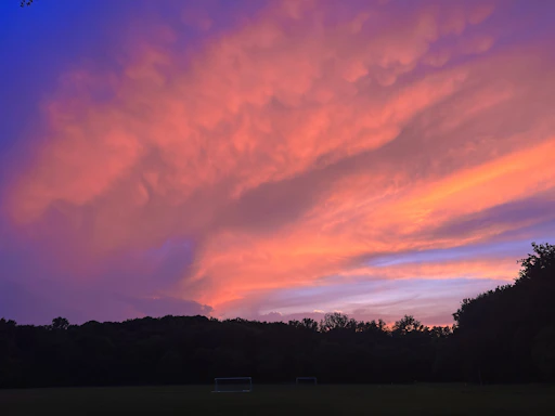 A vibrant photo of the women's football team celebrating a goal on the field at sunset.