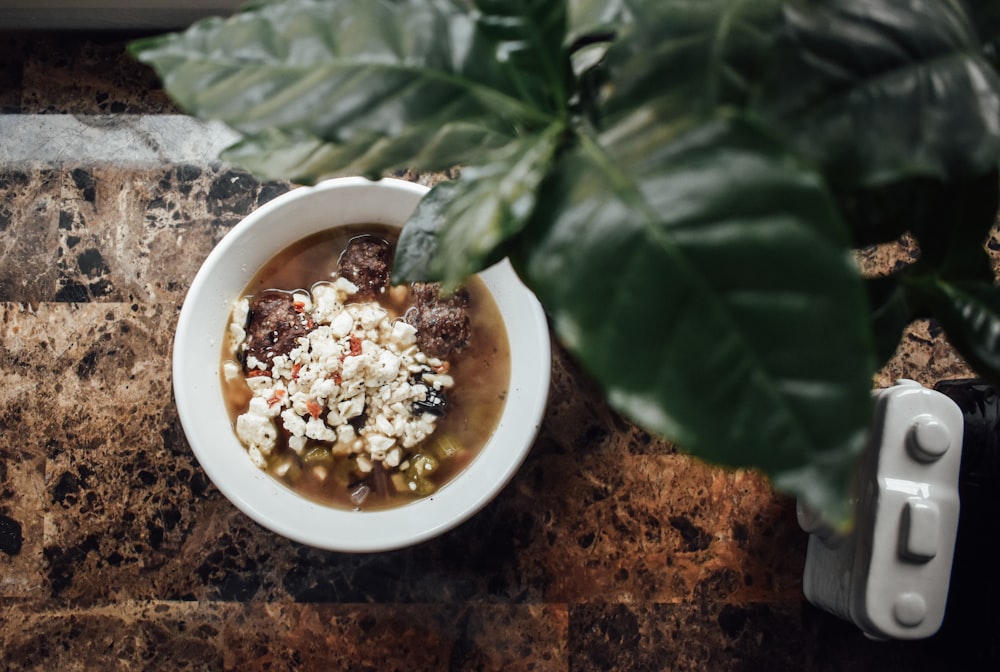 a white bowl filled with soup next to a green plant