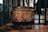 A highly decorative drum featuring a vibrant and intricate design filled with bold, colorful patterns. The design includes swirling shapes and stylized motifs in red, yellow, black, and white. The drum is situated in an industrial-looking space with metal and brick elements surrounding it.