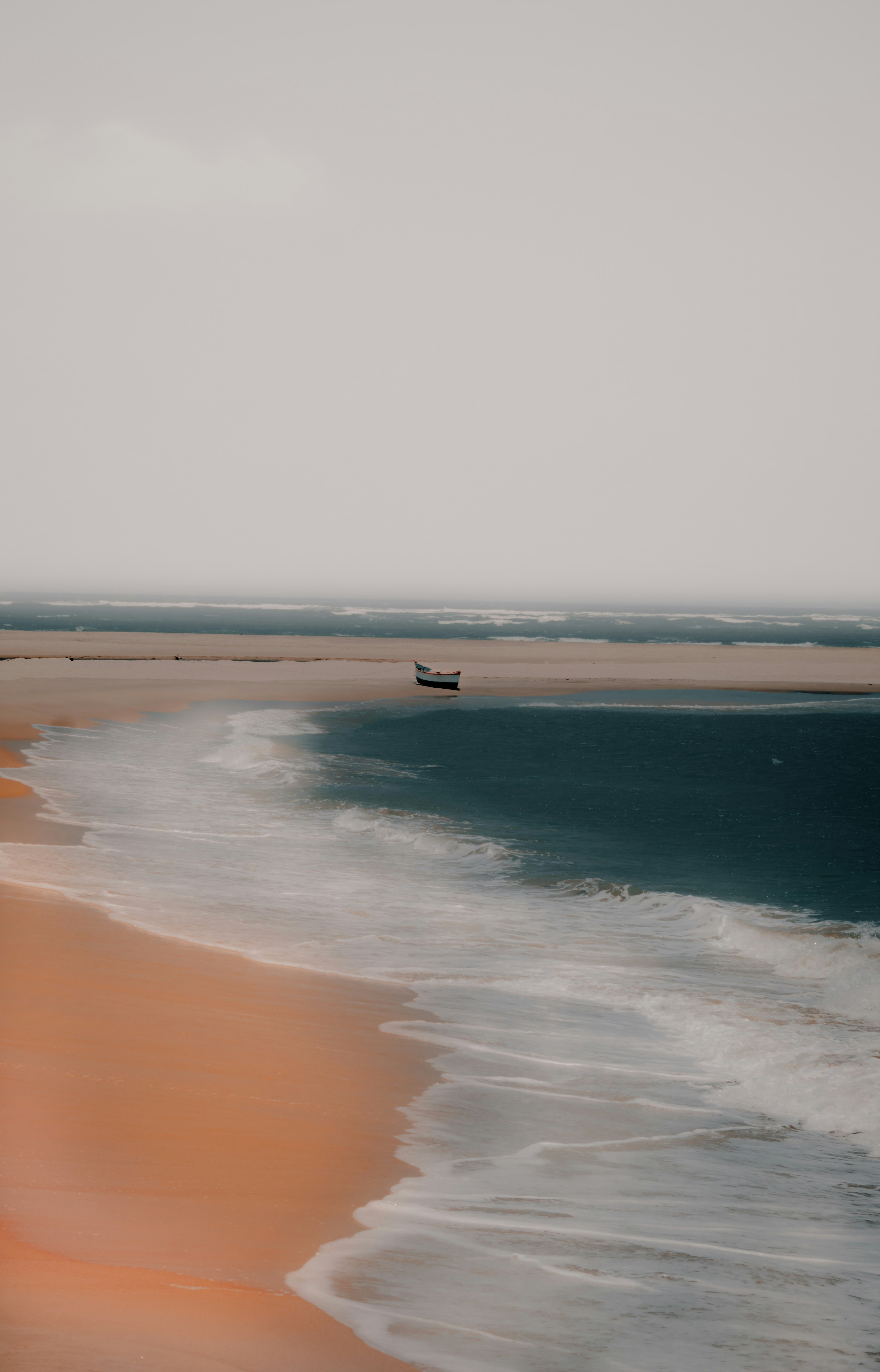 Sandy coastline with gentle waves and a small boat moored just offshore