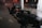 A professional video camera setup with multiple components including a monitor and various controls. The equipment features a detailed array of buttons and dials, and the environment has a subdued, low-light atmosphere with reflective surfaces.