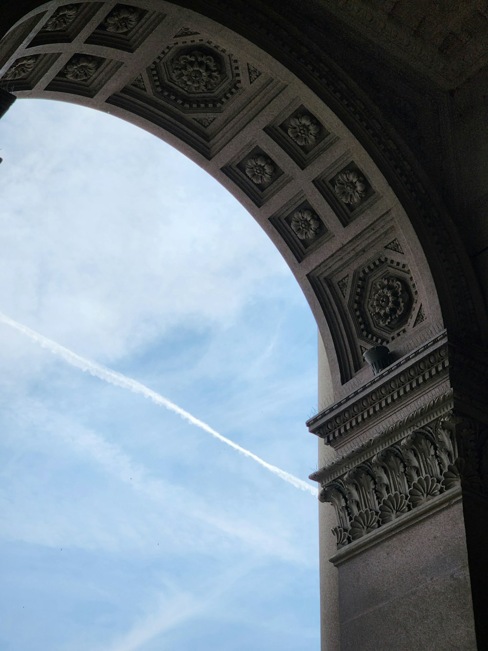 an arch with a plane flying in the sky