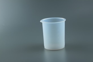 A translucent plastic measuring cup is placed against a plain gray background. The cup has a slightly frosted appearance with measurements faintly visible on its surface.