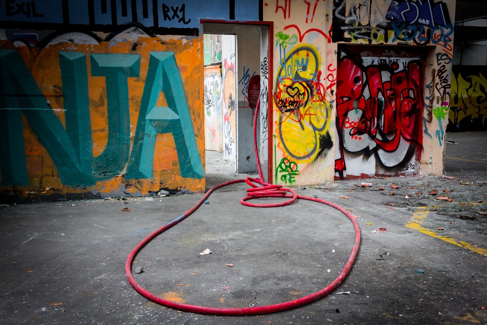a red hose is connected to a wall with graffiti
