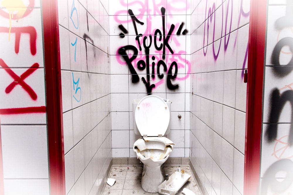 a white toilet sitting in a bathroom with graffiti on the walls