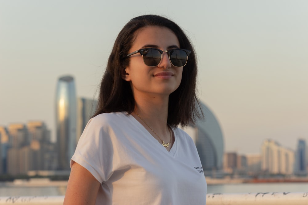 a woman wearing sunglasses standing in front of a body of water