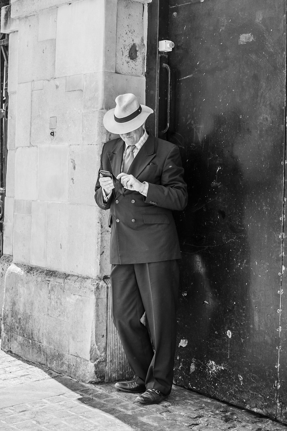 a man in a suit and hat leaning against a building