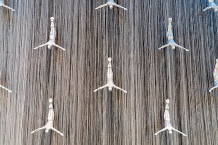 Silver statues of divers extend horizontally in a dramatic art installation against the backdrop of a cascading vertical water feature, creating a striking visual of movement and grace.