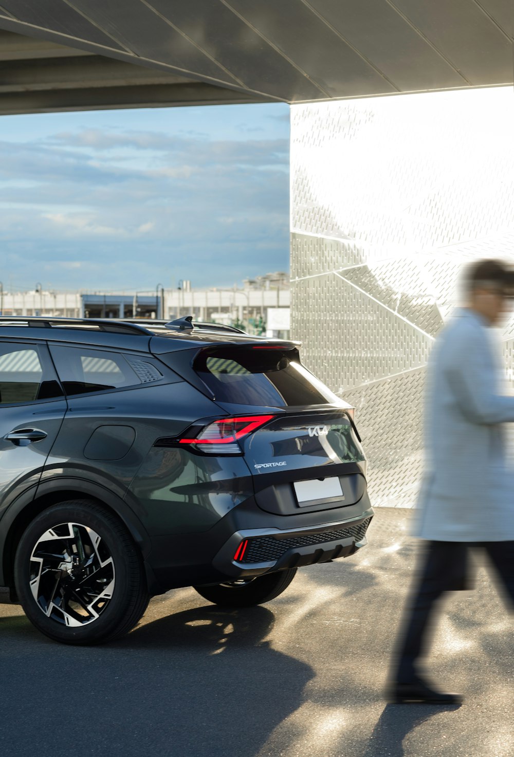 a woman in a white coat walking past a car