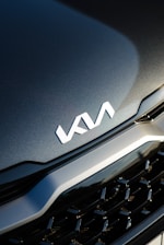 A close-up view of a car's front grille with the KIA logo prominently displayed. The surface appears sleek and polished, reflecting light subtly.