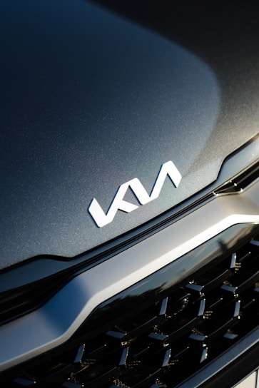 A close-up view of a car's front grille with the KIA logo prominently displayed. The surface appears sleek and polished, reflecting light subtly.