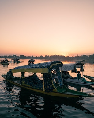 A serene view of Dal Lake at sunset with shikaras floating gently on the water.
