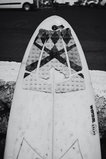 A sleek professional shortboard resting against a graffiti-covered wall on a sunny urban street.