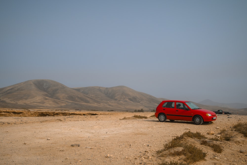 a red car parked in the middle of a desert