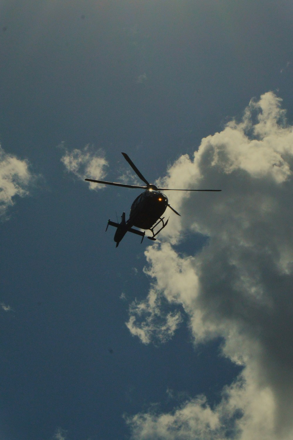 a helicopter flying through a cloudy blue sky