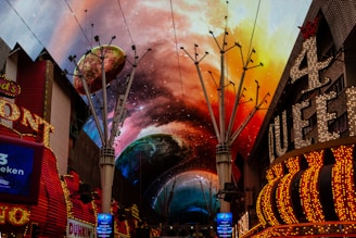 A vibrant and colorful canopy display features a cosmic theme with planets and nebulae in a city street. Neon signs and casino lights adorn the buildings, creating an electrifying atmosphere.