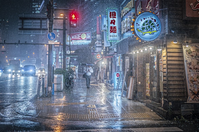 A moody nighttime street scene in Tokyo with glowing neon signs reflecting on wet pavement under a gentle rain.