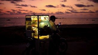 A delivery rider navigating through a bustling Guinean market street at sunset.