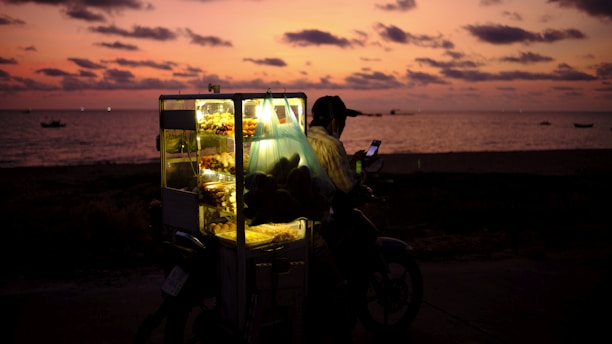 A delivery rider navigating through a bustling Guinean market street at sunset.