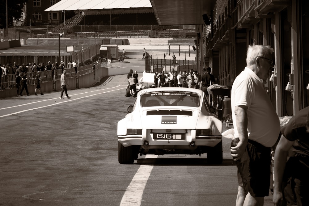 a white car driving down a street next to a crowd of people