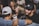 A group of people is gathered closely together, smiling and enjoying a social event. One person is holding a can, suggesting they are at a party or casual gathering. The atmosphere appears lively, with people engaging in conversation and laughter.
