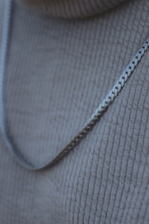 A close-up of a sleek silver chain necklace on a wooden surface.