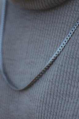 A sleek close-up of a silver chain necklace resting on a marble surface, reflecting soft natural light.