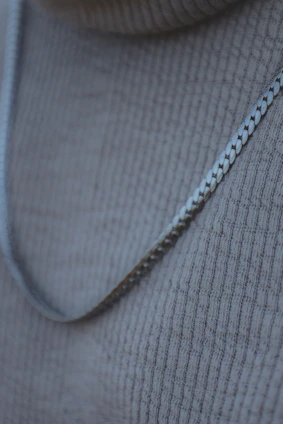 Close-up of a sleek silver necklace resting on a minimalist black fabric background, capturing urban chic.