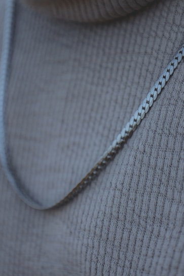 Close-up of a delicate silver necklace with intricate detailing resting on soft white fabric.