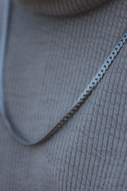 Close-up of a delicate silver necklace resting on soft beige fabric, bathed in natural light.