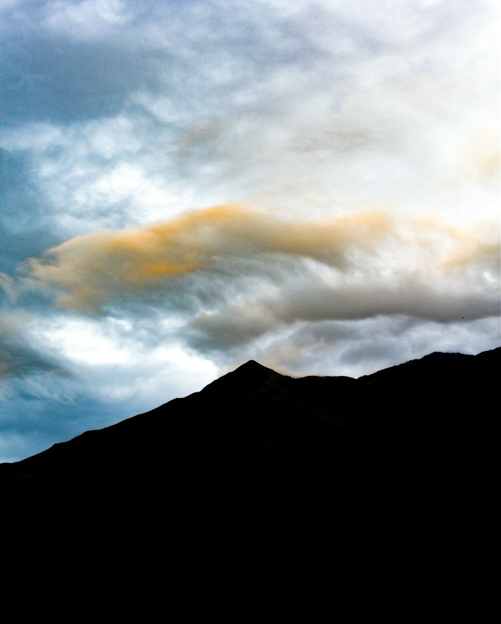 a plane flying over a mountain under a cloudy sky