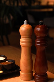 Close-up of a matte black salt and pepper grinder set on a natural wood tray