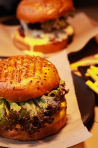 A close-up photo of a juicy burger with melted cheese, crispy fries on the side, set against a dark elegant background with yellow and red accents.