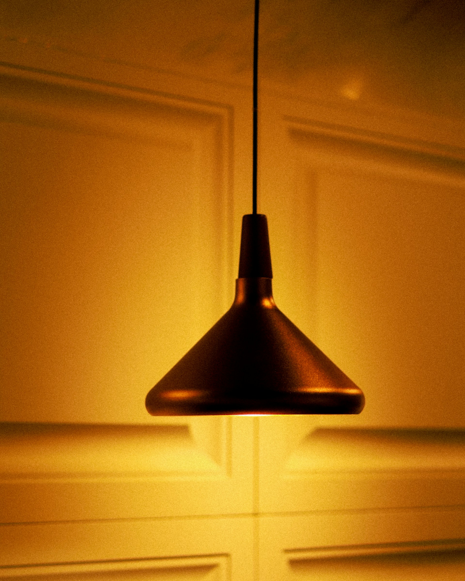A modern pendant lamp with a simple geometric shape casting warm light in a cozy room corner.