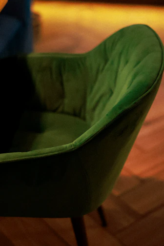 A cozy, classic wingback armchair upholstered in soft, deep green fabric with wooden legs.