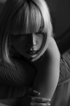 A monochrome photograph captures a person with short, straight hair. The lighting creates dramatic shadows across the face, emphasizing the contours and facial features. The overall mood is introspective and calm.