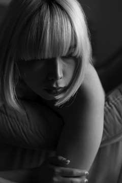 A monochrome photograph captures a person with short, straight hair. The lighting creates dramatic shadows across the face, emphasizing the contours and facial features. The overall mood is introspective and calm.