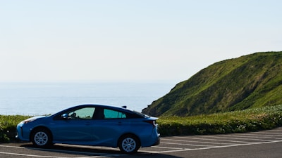 Compact car parked near a scenic coastal road under a clear blue sky.