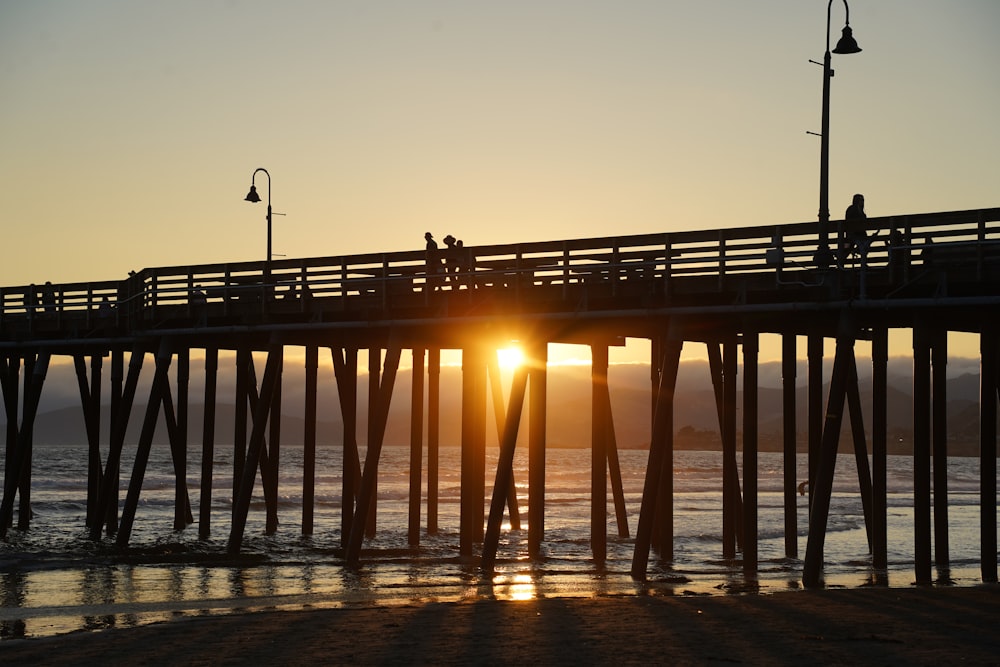 the sun is setting over a pier on the beach