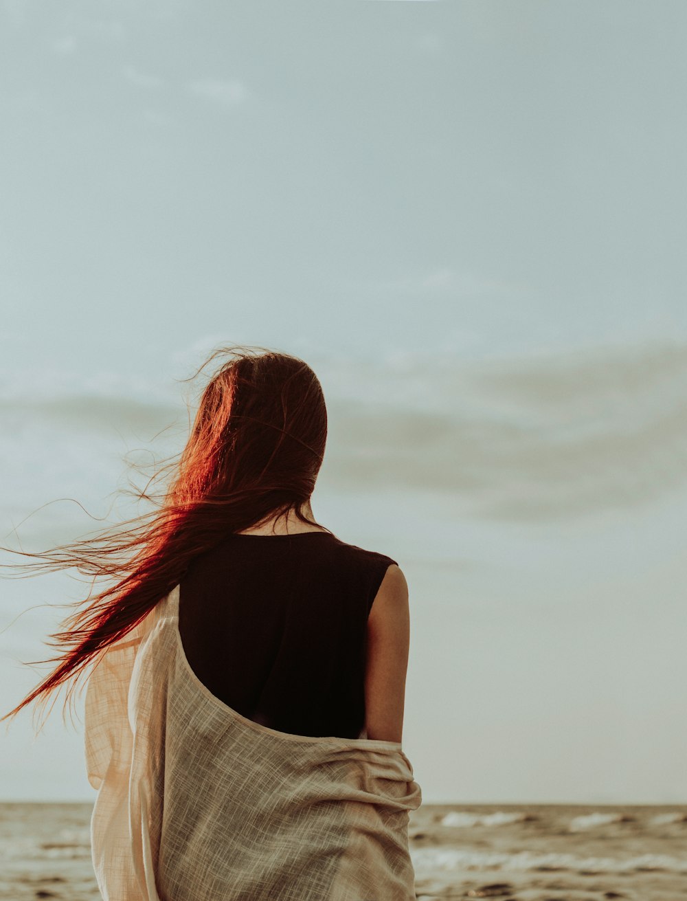 eine frau mit roten haaren, die am strand spazieren geht