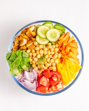 A vibrant zesty salad box with neatly arranged boiled pulses, fresh cucumber and carrot slices, and a lemon onion garnish in separate compartments.